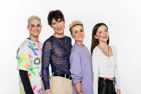smiling lgbtq community friends with rainbow flags on faces looking at camera isolated on grey