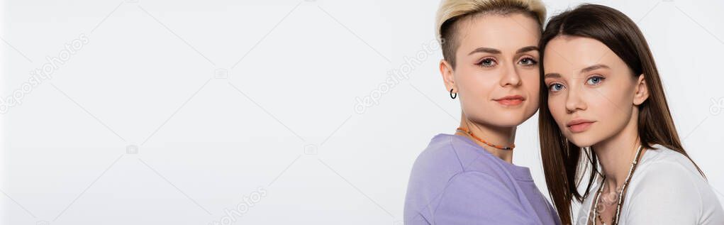 young and pretty lesbian women with makeup looking at camera isolated on grey, banner