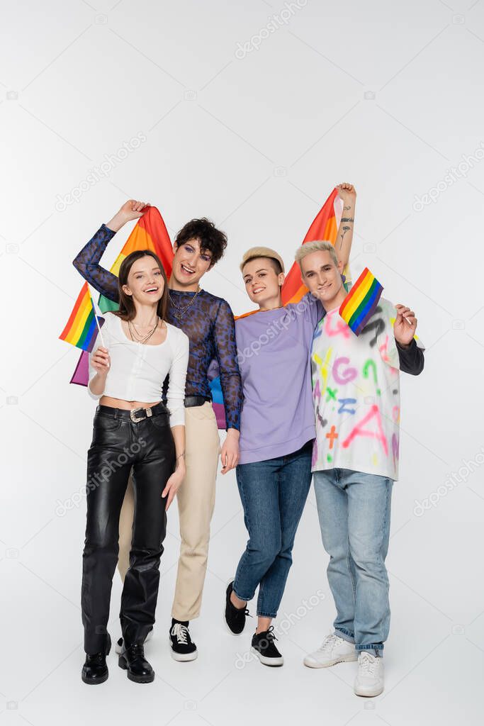 full length of joyful friends of diverse identity holding lgbtq flags on grey background