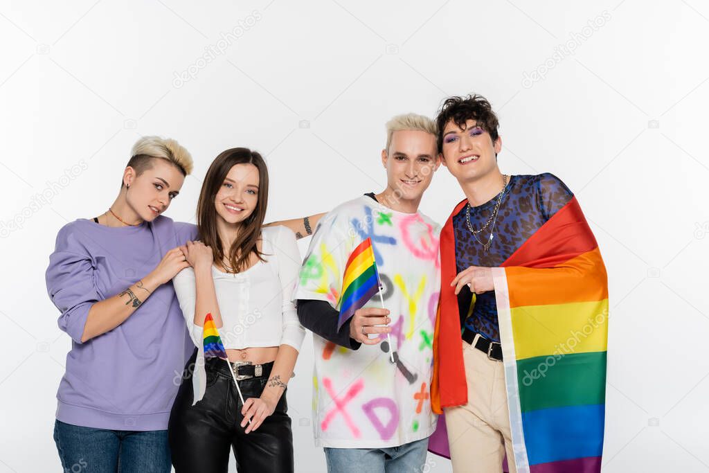 happy and stylish lgbtq community people with rainbow flags smiling at camera isolated on grey