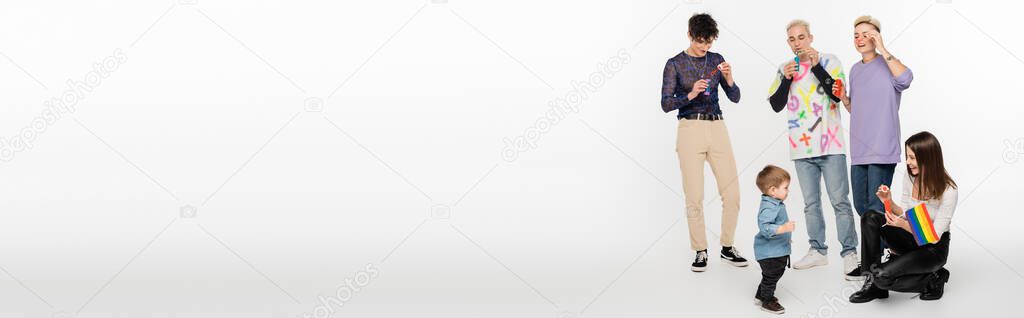 toddler boy near young lgbtq community friends blowing soap bubbles on grey background, banner