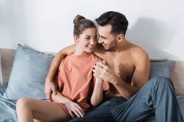 Mutlu genç çift el ele tutuşup birbirlerine yatakta bakıyorlar.