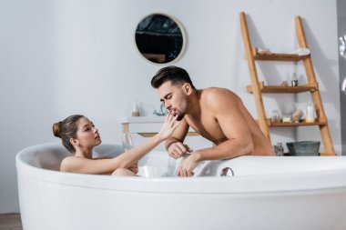 Seksi tişörtsüz erkek arkadaşının yanında sigara tutan baştan çıkarıcı kadın bir bardak şampanyayla banyoda dinlenirken...