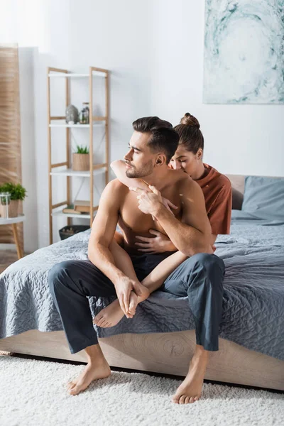 Σαγηνευτική Γυναίκα Αγκαλιάζει Γυμνόστηθο Άνδρα Παντελόνι Πιτζάμας Κάθεται Στο Κρεβάτι — Φωτογραφία Αρχείου