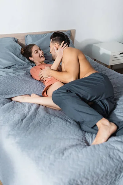 在家里 穿着睡衣裤的快乐女人抱着赤身裸体的男人躺在床上 — 图库照片