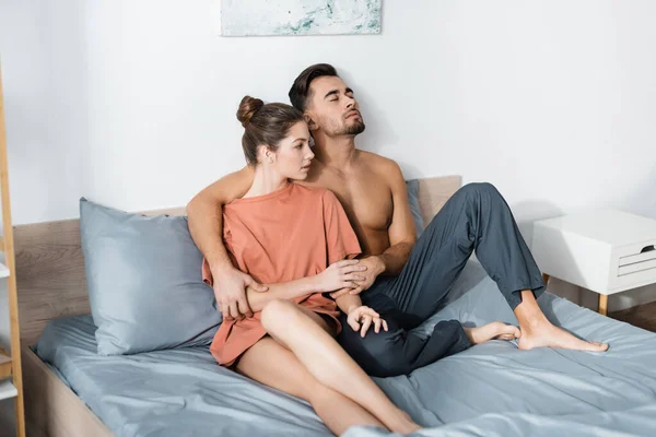 穿着睡衣裤子的肌肉男紧闭双眼坐在床上 手牵着女友的T恤衫 — 图库照片