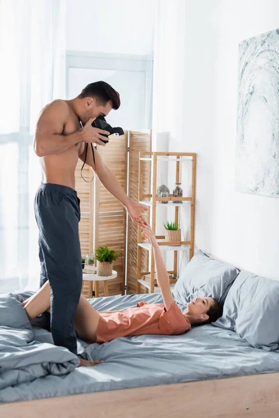 没穿衬衫的男人 带着老式相机 触摸着躺在灰色被褥上的女朋友的手 — 图库照片