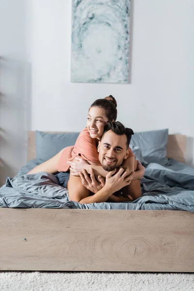Happy Man Looking Camera Girlfriend Hugging Him Bedroom — Stock Photo, Image