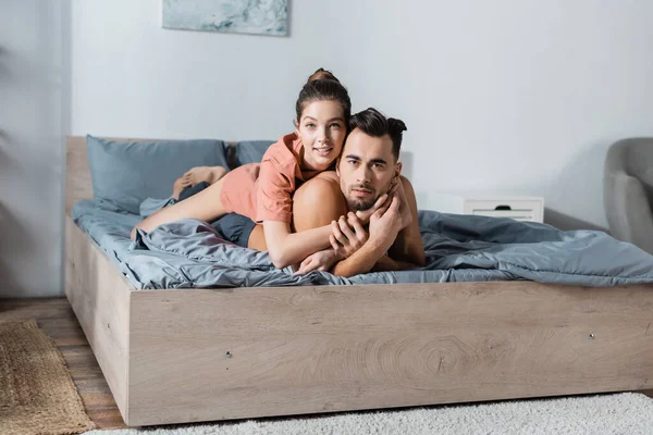 Young Sexy Couple Smiling Camera While Embracing Grey Bedding — Stock Photo, Image