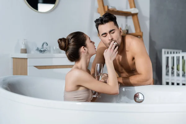 在浴缸里放松的时候 迷人的女人拿着香槟酒杯 边靠近男人边抽烟 — 图库照片