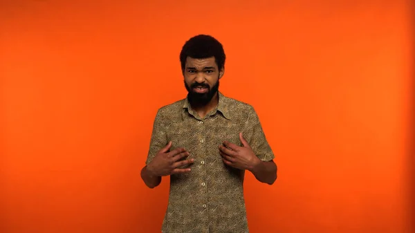 Uomo Afroamericano Incerto Camicia Guardando Fotocamera Mentre Indica Sfondo Arancione — Foto Stock