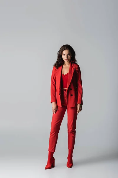 In voller Länge junge stilvolle Frau in roten Stiefeln und Anzug posiert auf grau — Stockfoto