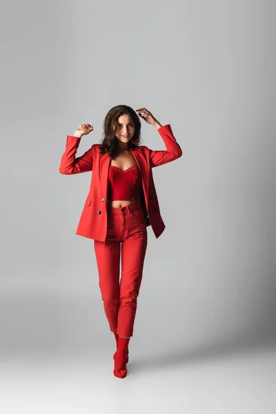 Full length of young pleased woman in red boots and suit posing on grey — Stock Photo