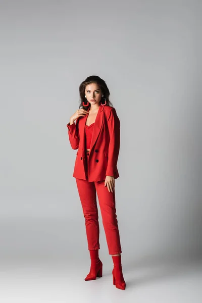 Full length of young woman in red boots and suit posing on grey — Stock Photo