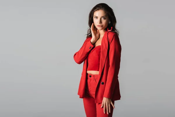 Jovem mulher elegante em terno vermelho e brincos posando isolado no cinza — Fotografia de Stock