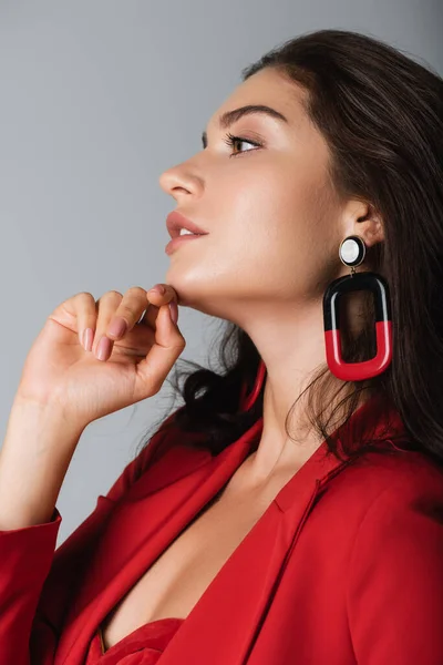 Vista laterale della donna alla moda in abito rosso e orecchino posa isolata sul grigio — Foto stock