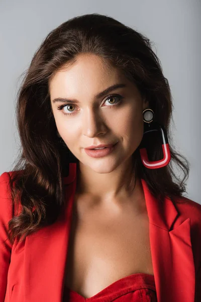 Heureux jeune femme à la mode en costume rouge et boucles d'oreilles posant isolé sur gris — Photo de stock