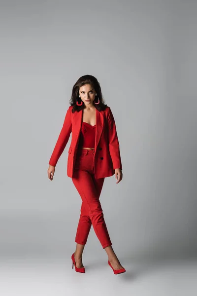 Полная длина молодая стильная женщина в красных каблуках и платье ходить по серому — стоковое фото