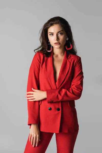 Mujer con estilo en traje rojo posando y mirando a la cámara aislada en gris - foto de stock