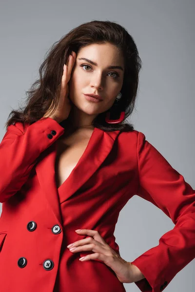 Tiefansicht einer stilvollen Frau im roten Anzug, die mit der Hand auf der Hüfte posiert und isoliert auf grau in die Kamera blickt — Stockfoto