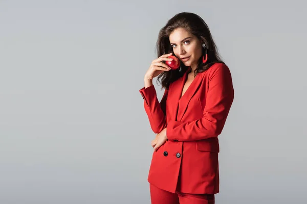 Young woman in red suit posing with fresh apple isolated on grey — Stock Photo