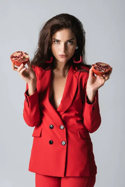 Femme élégante en costume tendance tenant des moitiés de grenade rouge isolé sur gris — Photo de stock