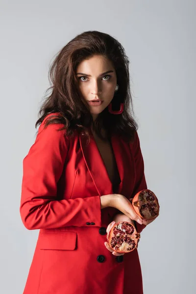 Brunette woman in trendy suit holding red pomegranate isolated on grey — Stock Photo