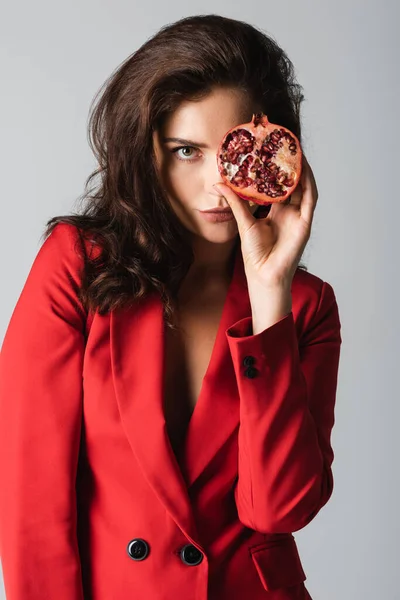 Young woman in suit holding red pomegranate half isolated on grey — Stock Photo