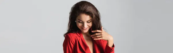Fröhliche junge und brünette Frau im roten Anzug isoliert auf grau, Banner — Stockfoto