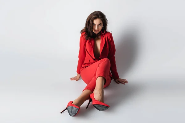 Pleine longueur de jolie femme en costume rouge posant tout en étant assis sur gris — Photo de stock