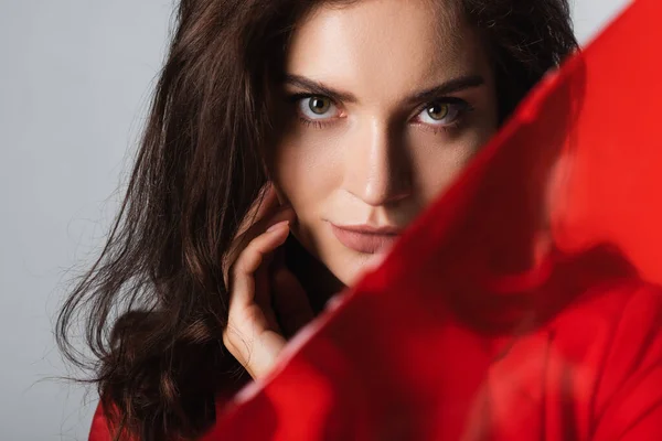 Young woman looking at camera near blurred red glass isolated on grey — Stock Photo