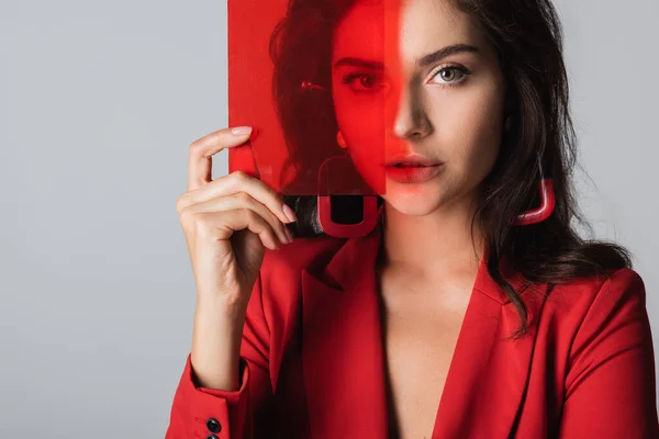 Brunette young woman looking at camera and holding red glass isolated on grey — Stock Photo