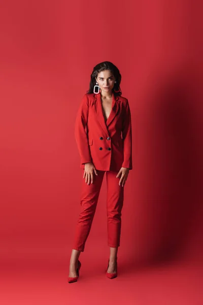 Full length of young brunette woman in suit posing on red — Stock Photo