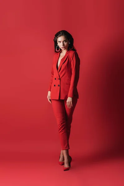 Longitud completa de la joven modelo morena en traje posando en rojo - foto de stock