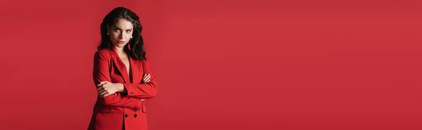 Young brunette model in suit posing with crossed arms isolated on red, banner — Stock Photo