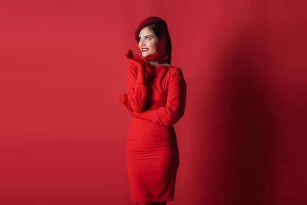 Happy and elegant woman in beret and dress posing on red — Stock Photo