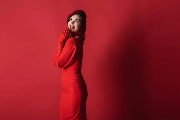 Mujer alegre y elegante en boina y vestido posando sobre rojo - foto de stock