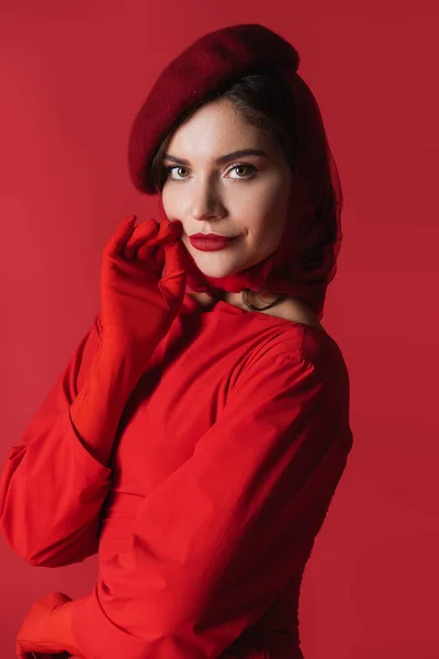 Femme élégante en béret et robe regardant la caméra isolée sur rouge — Photo de stock