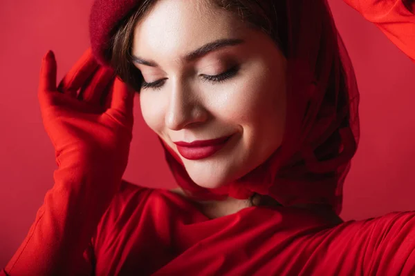 Close up of smiling young woman adjusting beret isolated on red — Stock Photo