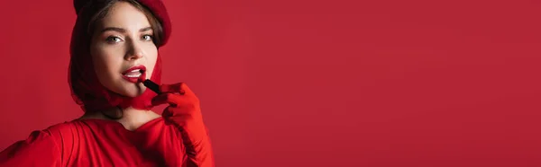 Young woman in glove, headscarf and beret applying lipstick isolated on red, banner — Stock Photo