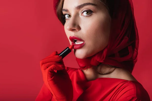 Young woman in glove and beret applying lipstick isolated on red — Stock Photo