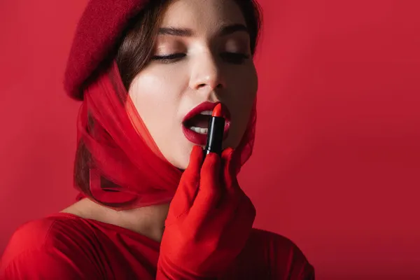 Bonita mujer con la boca abierta aplicando lápiz labial aislado en rojo - foto de stock