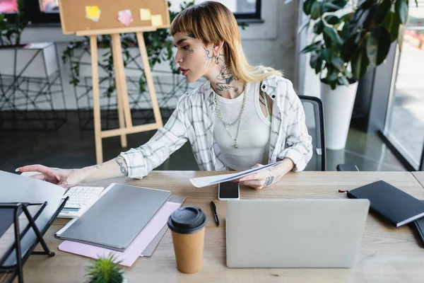 Mulher de negócios na moda com corpo tatuado trabalhando com documentos perto de laptop no escritório — Fotografia de Stock