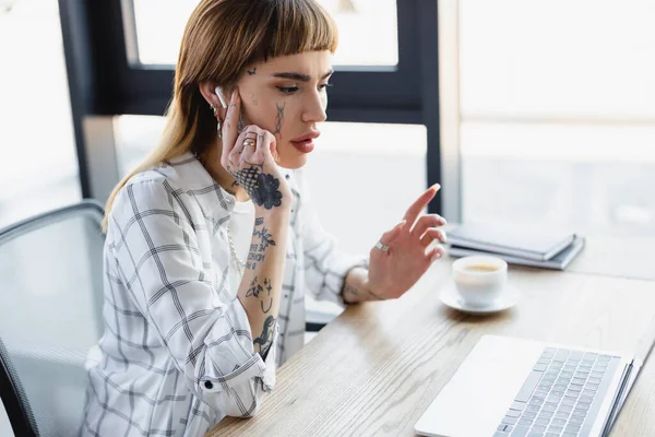 Tattooed woman in earphone sitting at workplace during video conference on laptop — Stock Photo