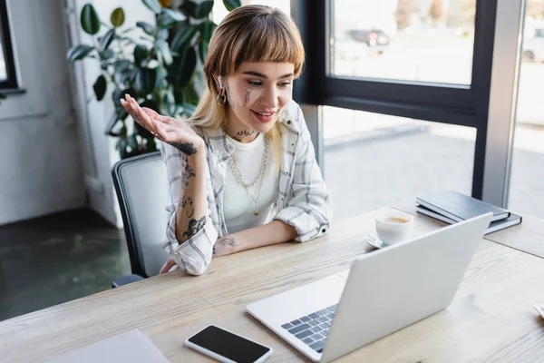 Stylish and positive businesswoman pointing with hand during video conference on laptop in office — Stock Photo