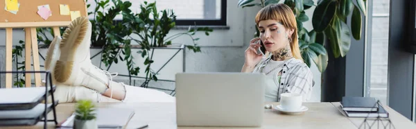 Mujer de negocios de moda sentada con piernas en el escritorio mientras habla por teléfono móvil, pancarta - foto de stock