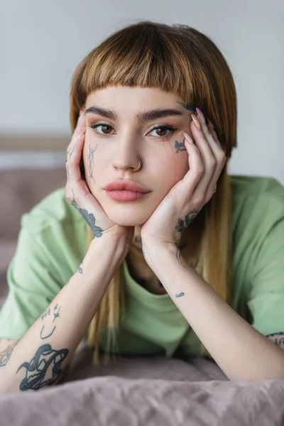 Pretty young woman with tattooed face and hands looking at camera at home — Stock Photo