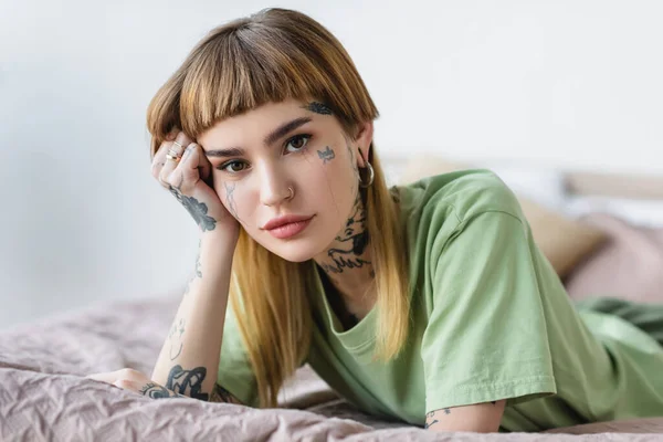 Молодая татуированная женщина смотрит в камеру, когда лежит на кровати — стоковое фото