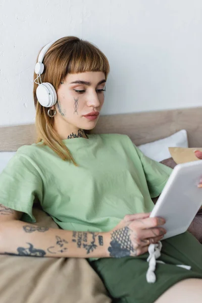 Femme tatouée tenant tablette numérique tout en écoutant des leçons en ligne dans les écouteurs à la maison — Photo de stock
