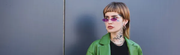 Молода татуйована жінка в окулярах і зеленому піджаку дивиться на відкритому повітрі, банер — Stock Photo